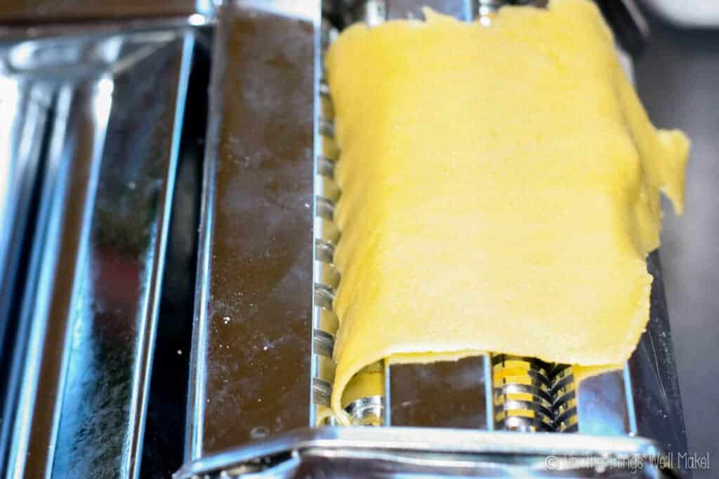 closeup overhead view of pasta being cut in the cutting attachment for making pasta noodles.