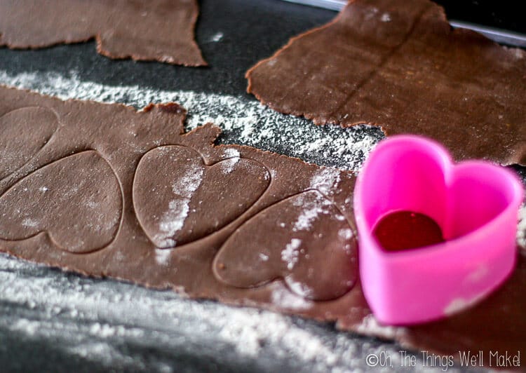Close up of a strip of chocolate pasta with heart shaped markings and pink heart shaped cookie cutter at the right end.