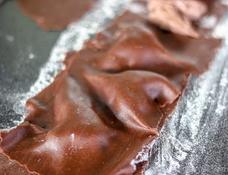 Adding another layer of chocolate pasta over the chocolate mascarpone filling, and gently molding it to shape the ravioli