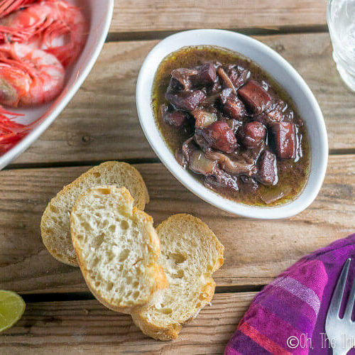 Calamares al vino tinto, or red wine braised squid, as seen from above served with bread and red prawns