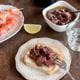 A plate of red wine braised squid on top of a slice of bread with a plate of shrimp, slice of lemon, and a bowl of squid in the background.