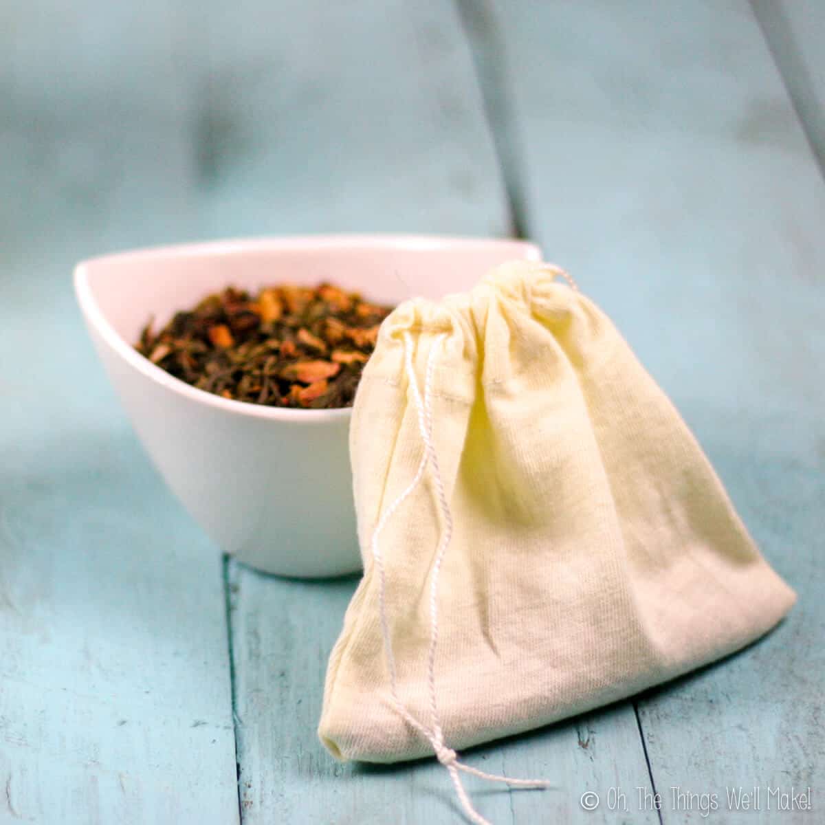 Closeup of a homemade cloth teabag with a small bowl behind it filled with a loose tea.