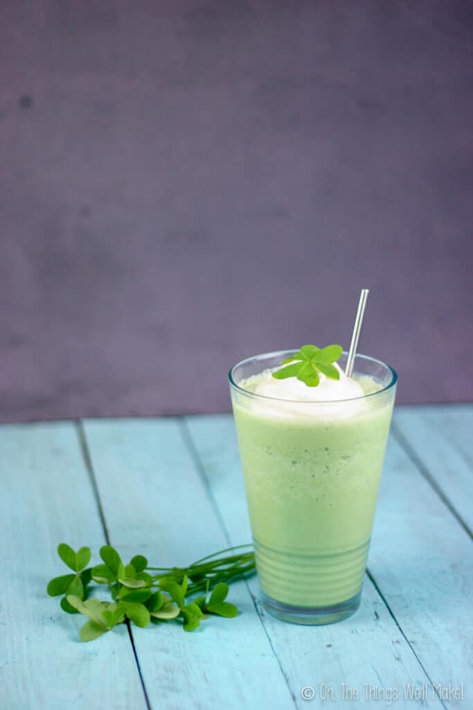 Naturally colored and flavored homemade shamrock shake next to a bunch of clovers and topped with whipped cream and a clover for garnish.
