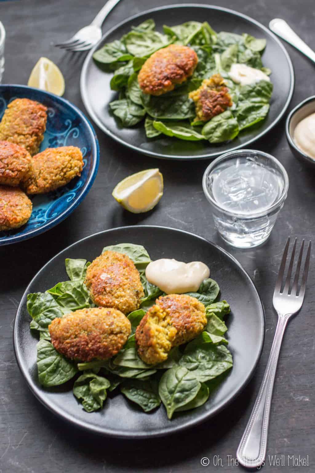 Several plates full of pieces of turmeric falafels placed on top of leafy greens with a dollop of sauce on the side.
