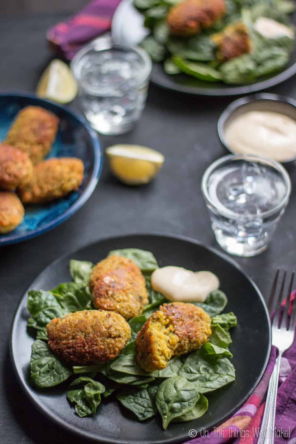 Several plates full of pieces of turmeric falafels placed on top of leafy greens with a dollop of sauce on the side.