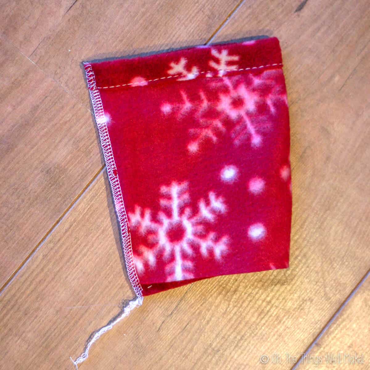 Top view of a red with white snowflakes polar fleece sleeve after having the edges sewn together.