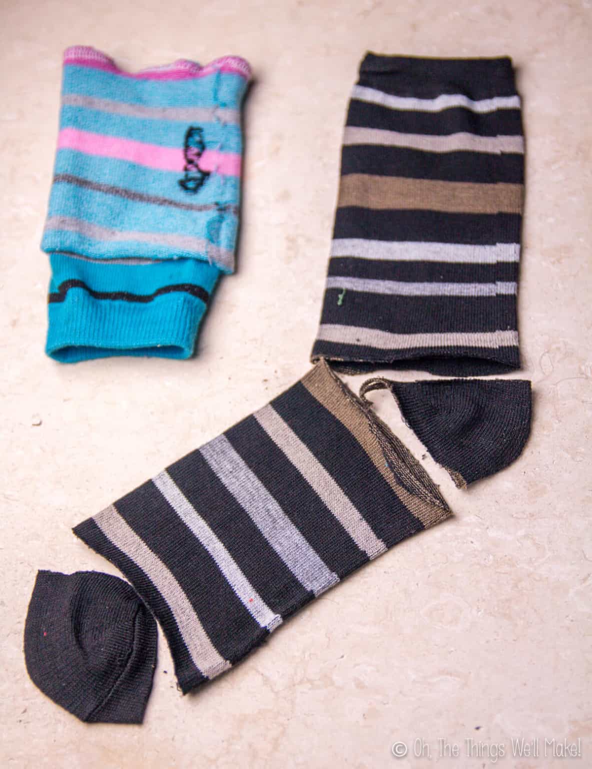 Top view of a black sock whose heel and toe areas have been cut out, and a blue sock that has been cut out and laid inside out.