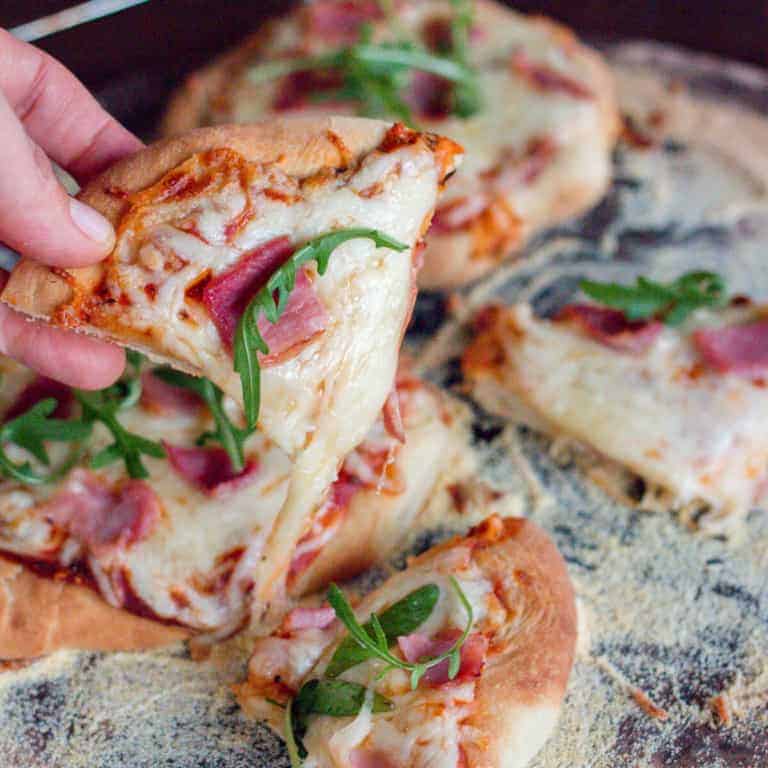 Close-up of a slice of mini pizza made out of homemade pizza dough. Pizza is filled with cheese, piece of meat and leafy greens.