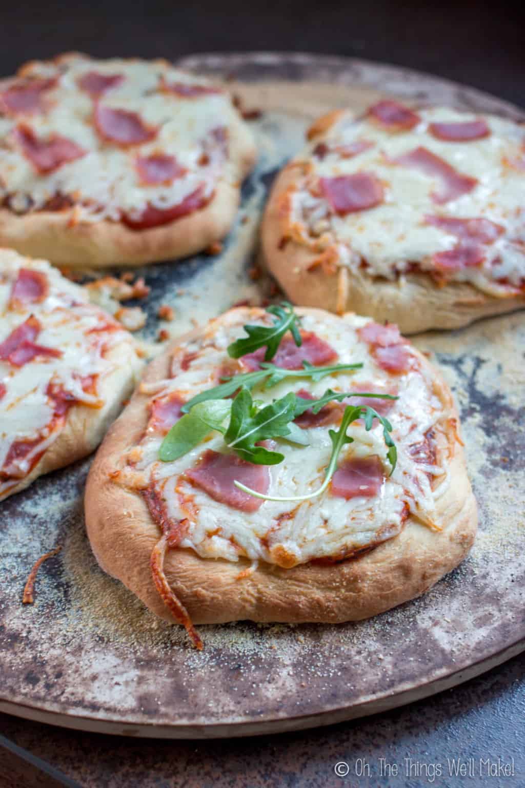 Close up of four individual mini sized pizzas on a ceramic pizza stone.