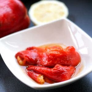 A small bowl of roasted red peppers in their juices, in front of a raw, whole red pepper.