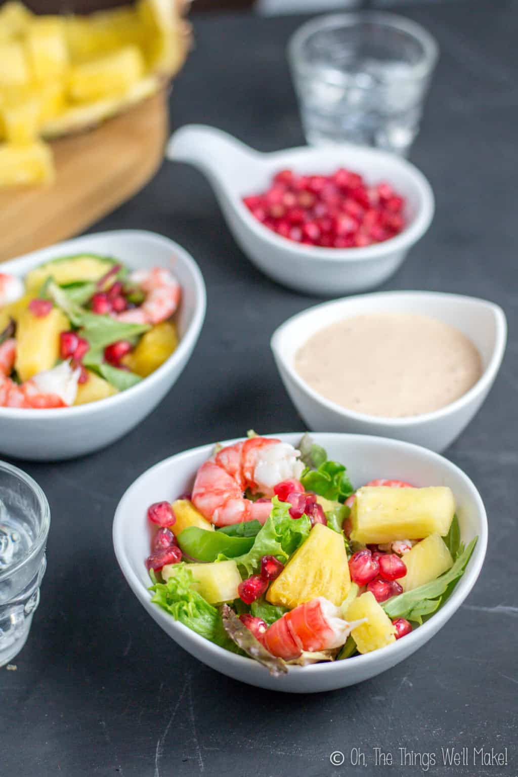 A white bowl of seafood salad in front with a bowl of salsa rosa in the back with another bowl of seafood salad beside it and a bowl of pomegranates at the back.