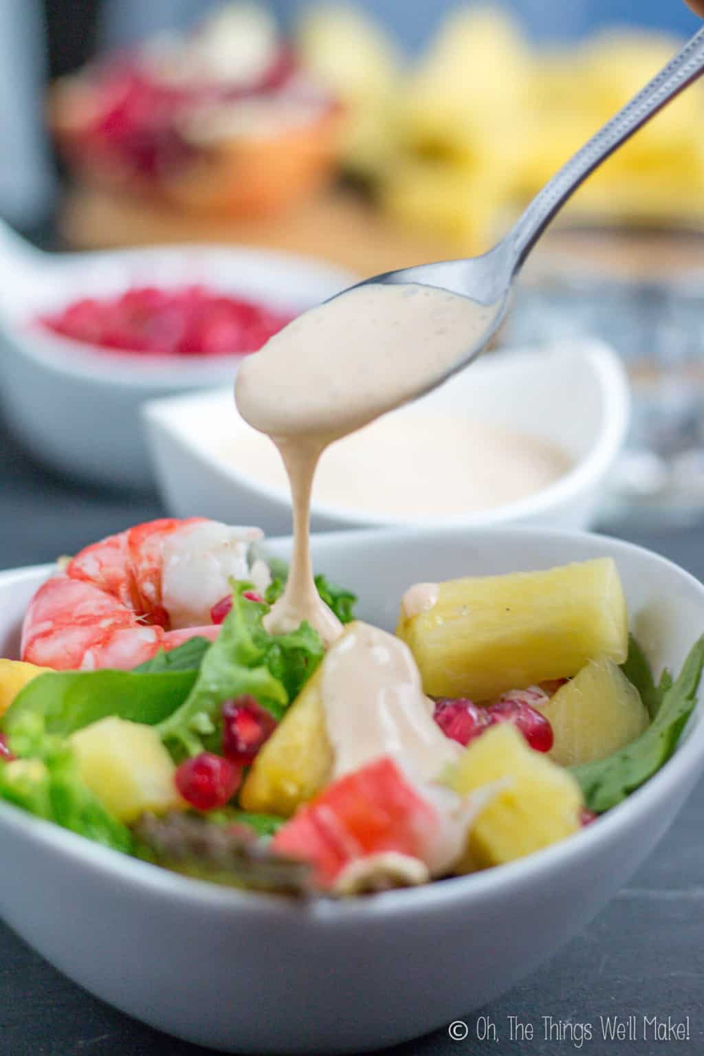 Close up of a spoon full of salsa rosa being poured over fresh salad.