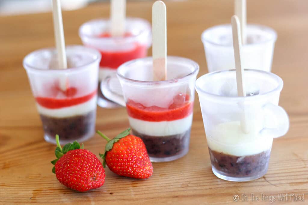 Cups with a blue layer covered with a white yogurt layer and a red strawberry layer on top.