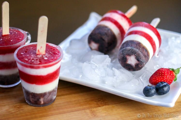 Some red, white, and blue popsicles on a platter, next to two that are still in their molds