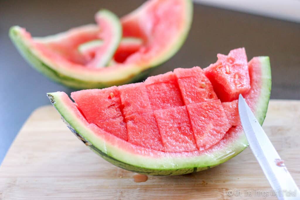 a piece of watermelon being cut up into chunks for freezing.