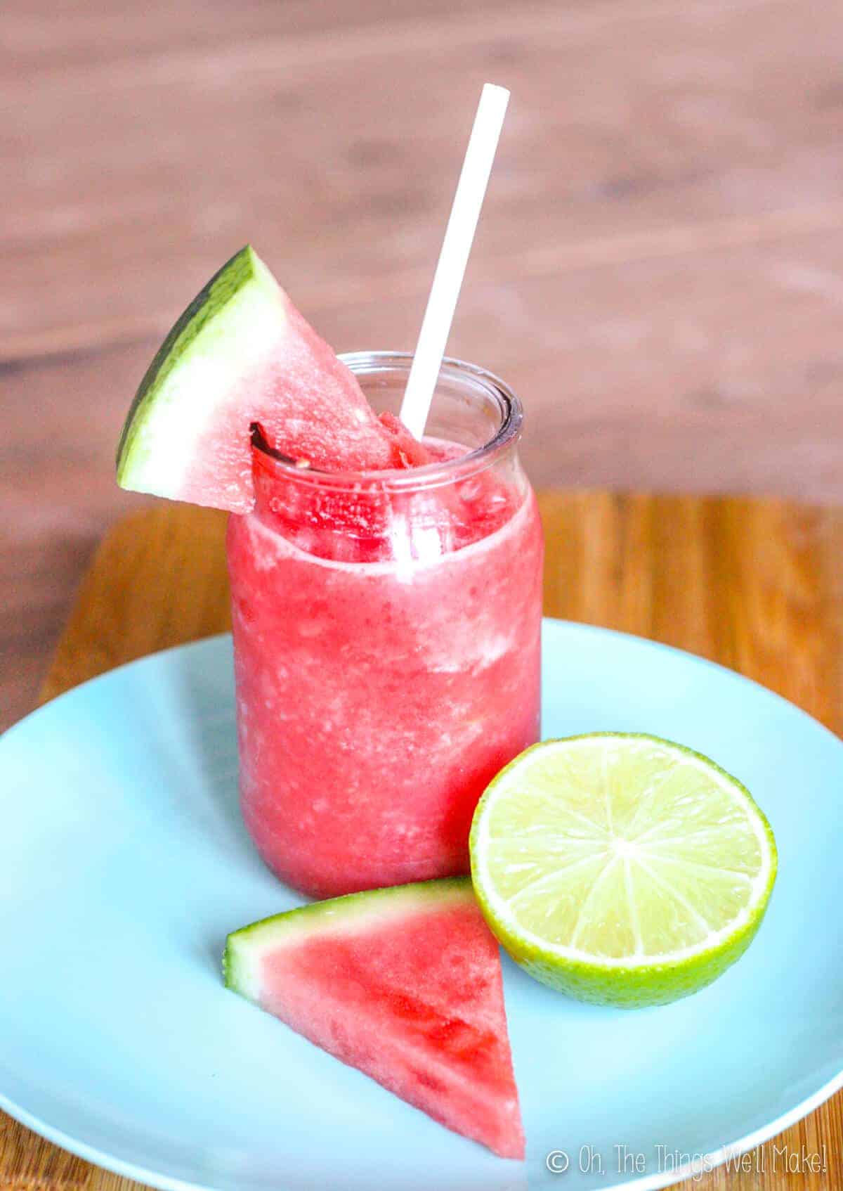 A watermelon slush on a plate with some watermelon and a lime slice.