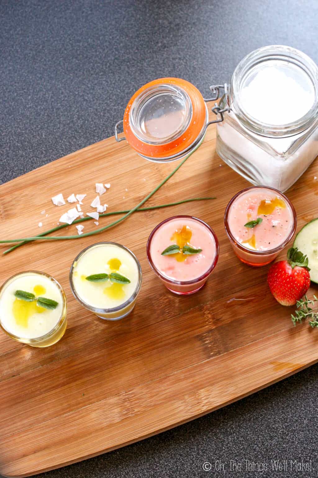 Overhead view of 4 shot glasses filled with a chilled gazpacho soup. The two on the left are green, the two on the right are pink. All are garnished with mint.