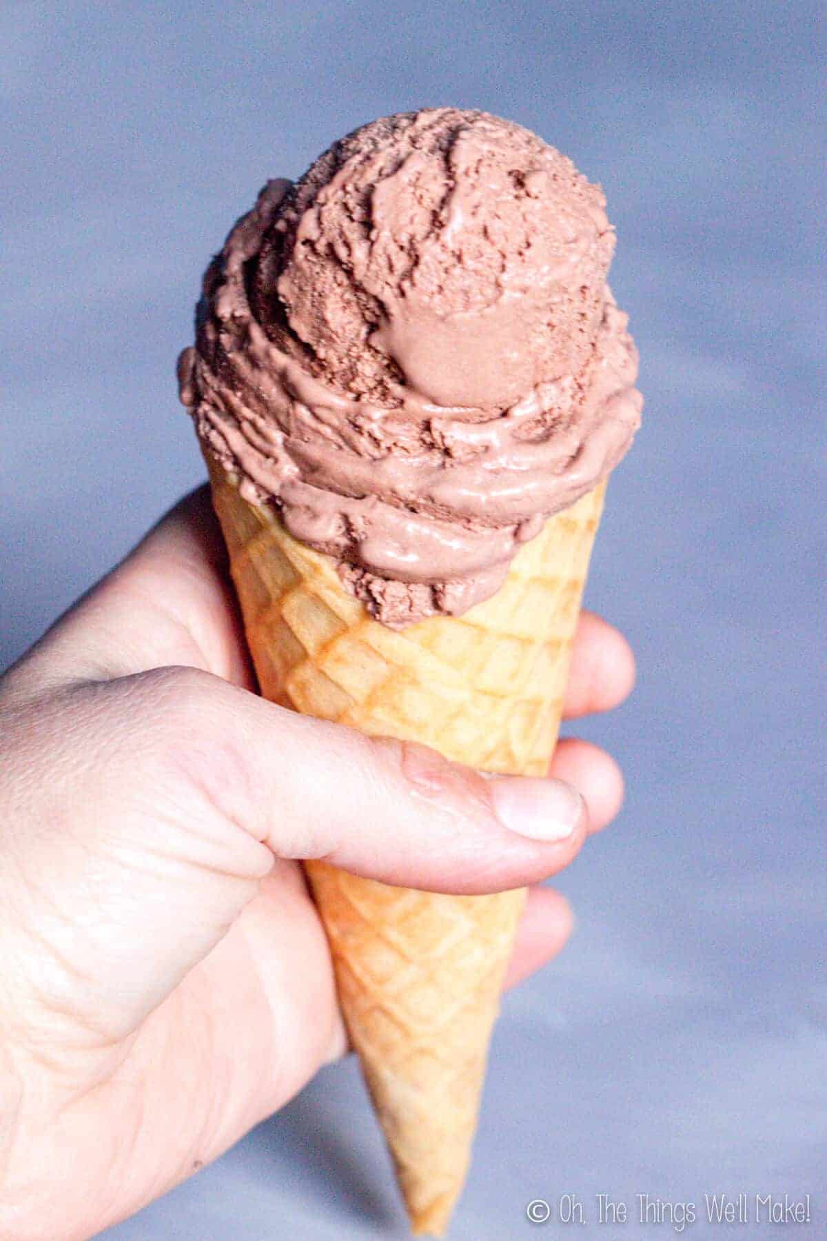 Closeup of a hand holding a chocolate ice cream cone in a homemade waffle cone.