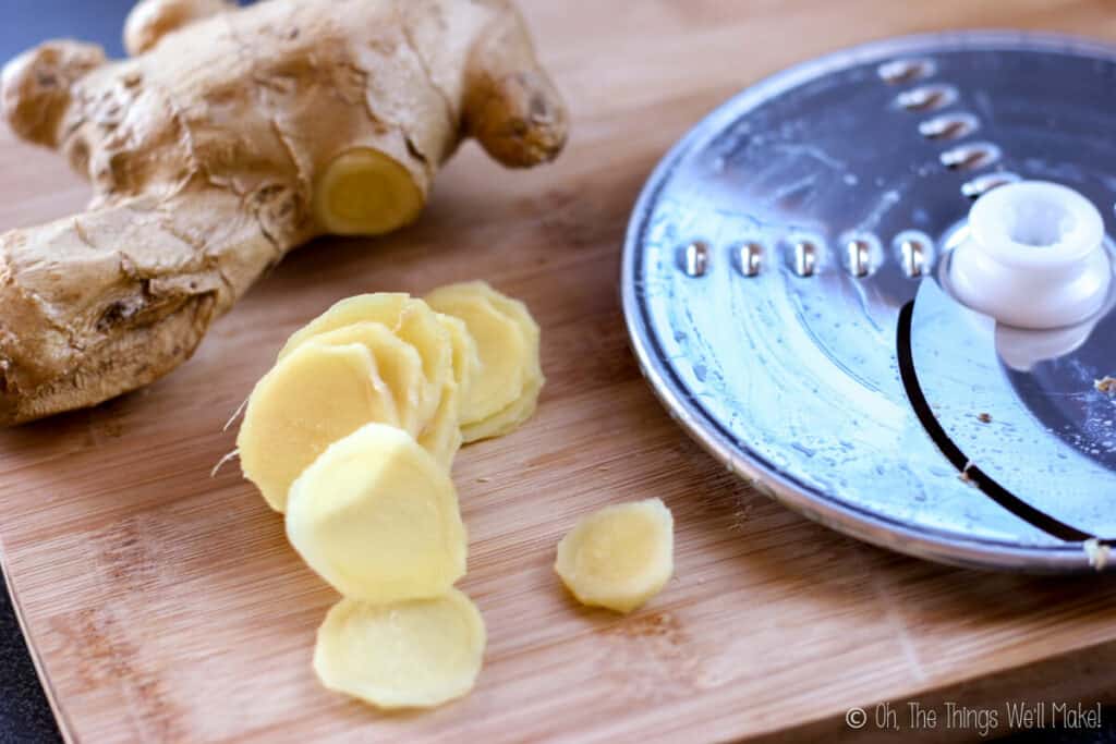 Slices of ginger root on a bamboo cutting board next to a slicing disk for a food processor.
