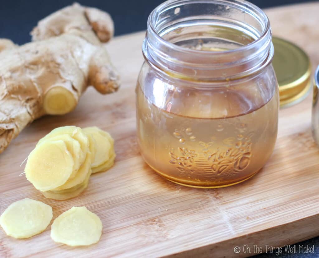 A jar with vinegar and sugar next to vinegar slices on a bamboo cutting board.