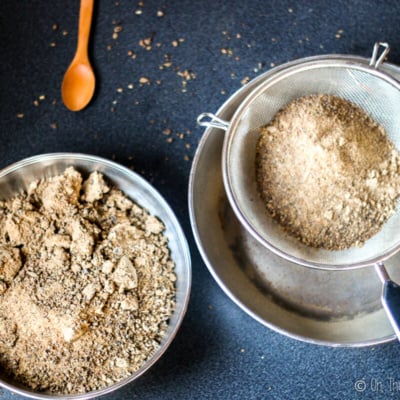 Overhead view of carob flour being sifted with a metal strainer