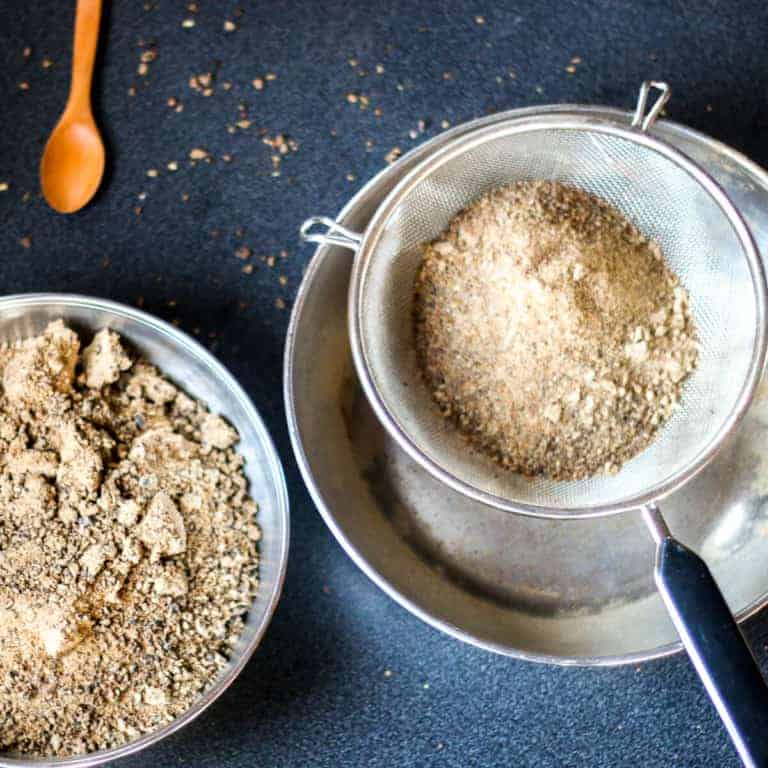 Overhead view of carob flour being sifted with a metal strainer