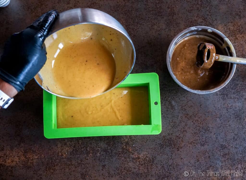 Pouring a light colored soap mixture into a silicone soap mold.