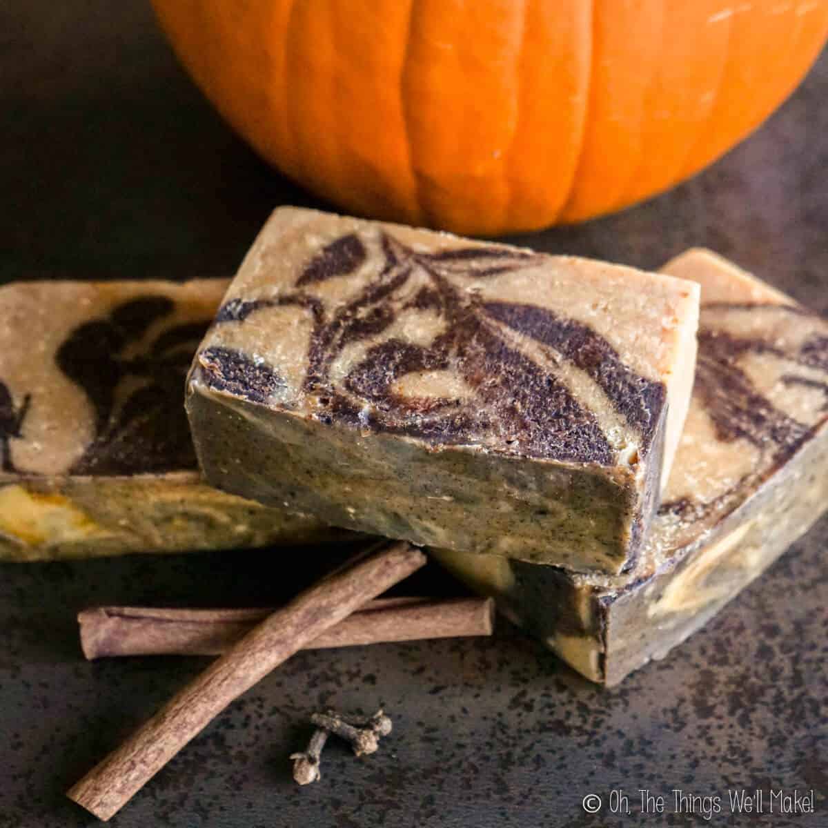 Overhead view of 3 bars of pumpkin spice soap surrounded by dried spices and a pumpkin