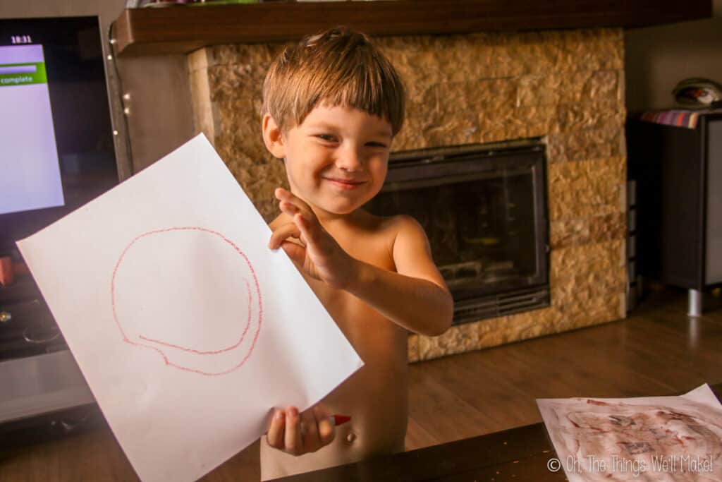 a boy holding a sheet of paper with a smiley face painted on it.