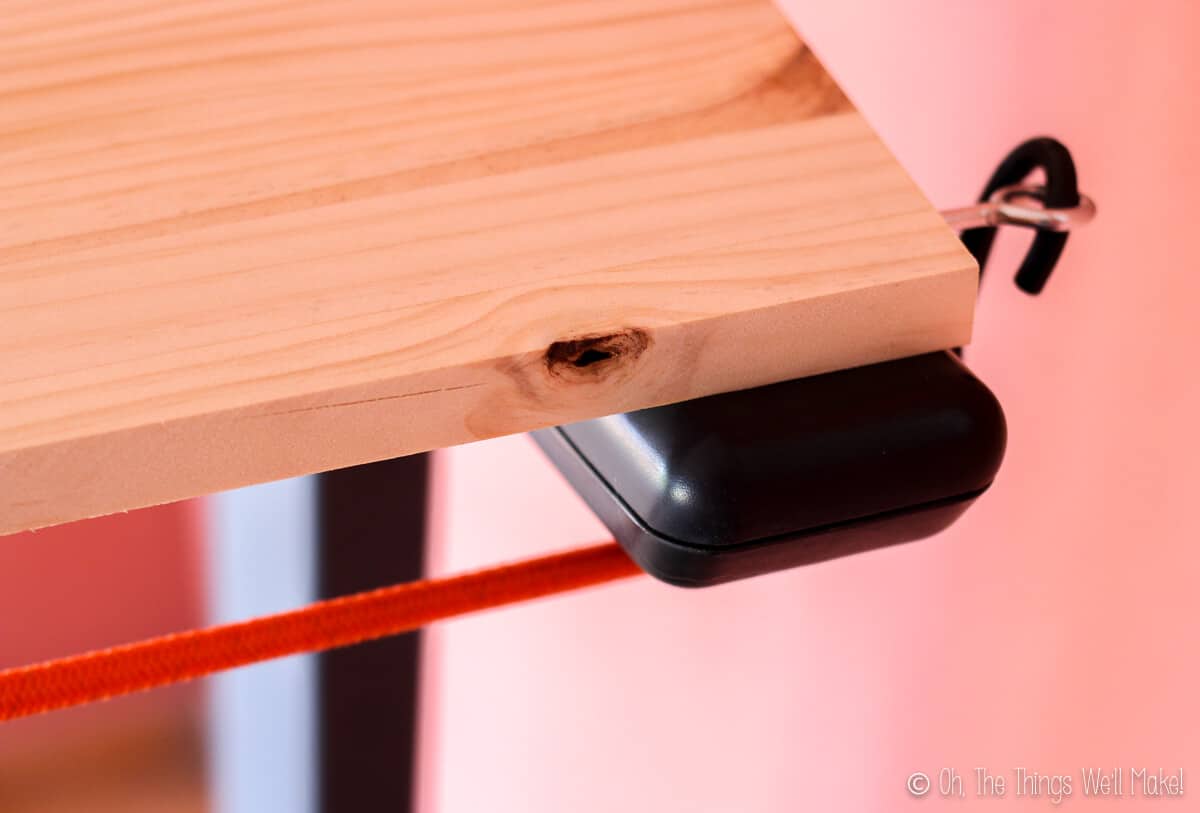Closeup of the front right area of a homemade treadmill desk showing how it's attached with a bungee cord in an eye hook.