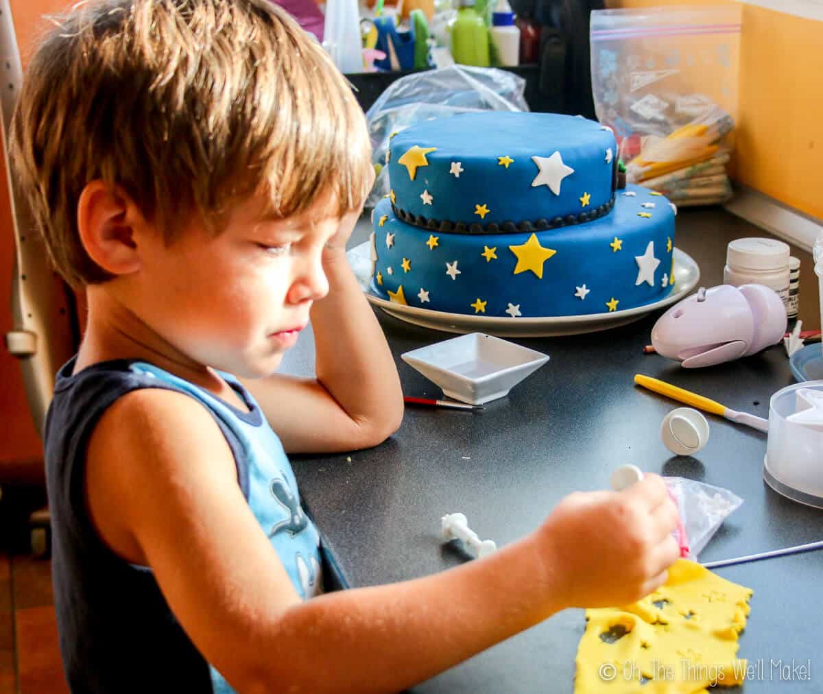 A young boy cutting out stars with a stamp on a piece of yellow fondant.