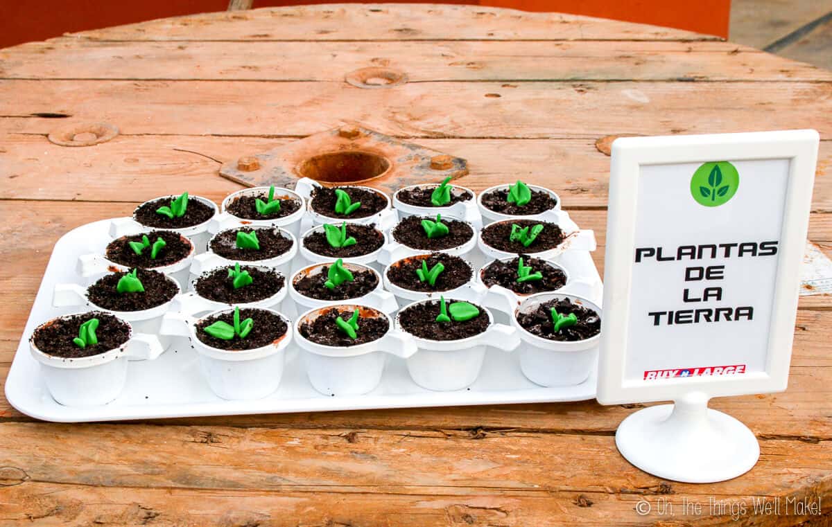 A tray full of handmade plants dessert which is crushed oreo placed on top of cups full of ice cream with a picture frame on the side saying "plantas de la terra."