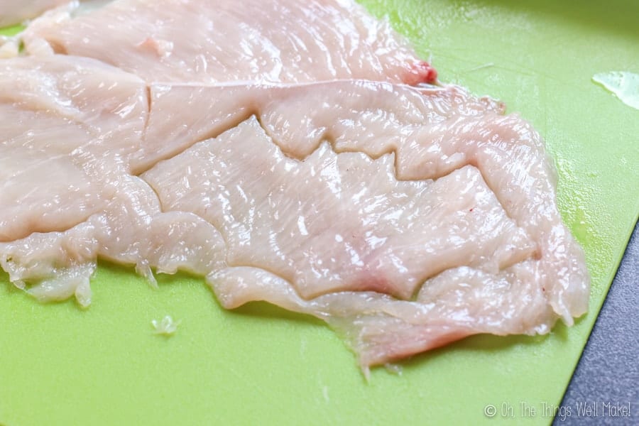 Bat-shaped piece of chicken breast being cut from the rest.