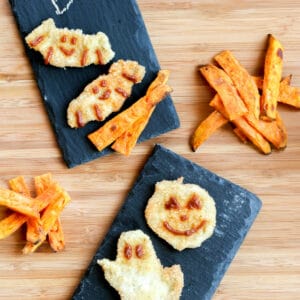 Halloween chicken nuggets shaped like ghosts, pumpkins, and bats, decorated with BBQ sauce and served with sweet potato fries.