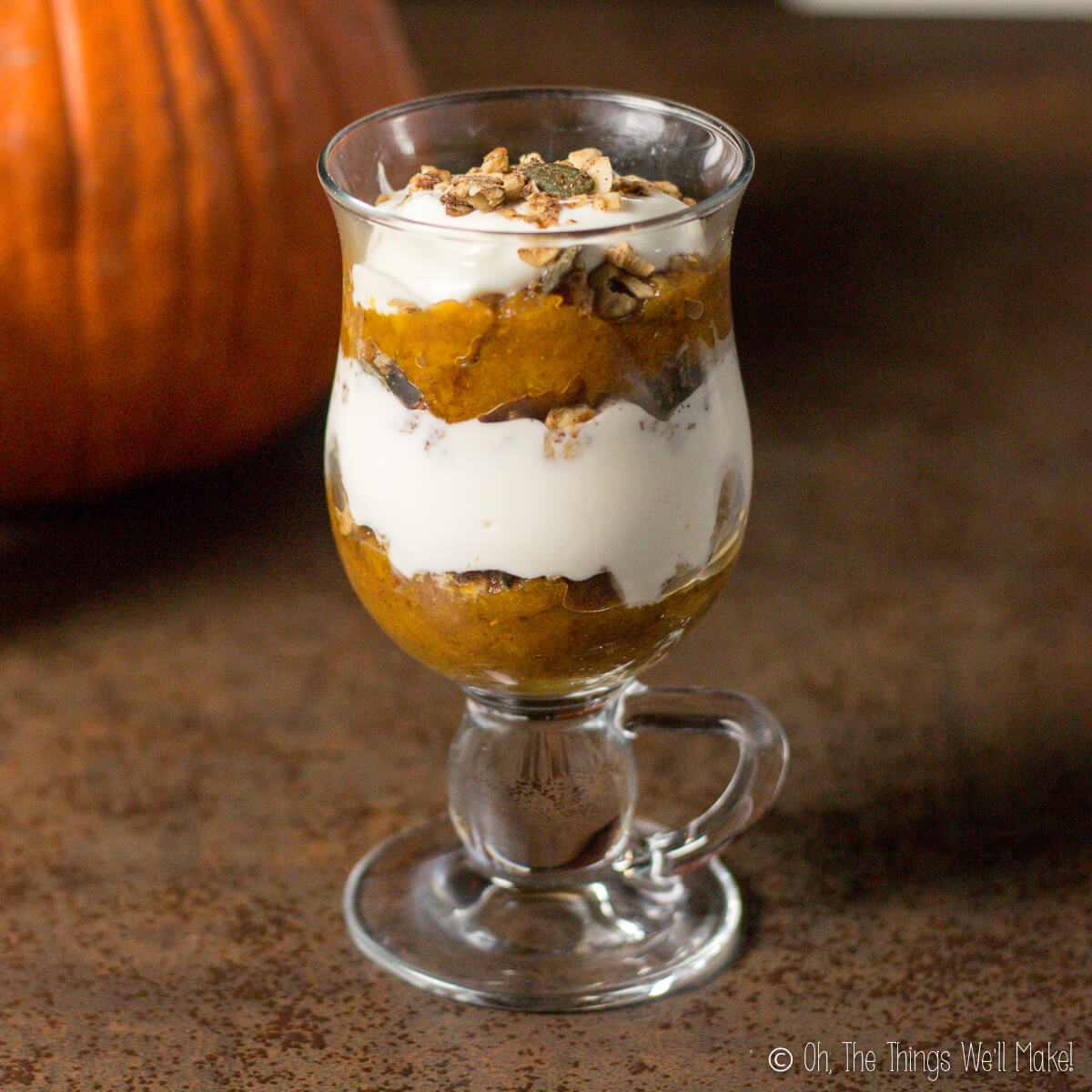 A clear glass full of pumpkin pie yogurt parfait showing off the layers of yogurt, pumpkin pie, and nuts.