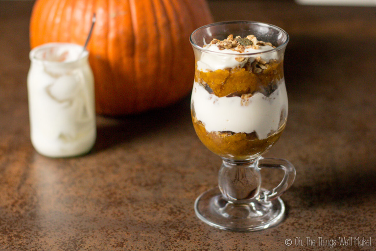 A pumpkin spice parfait in front of a jar of yogurt and a pumpkin