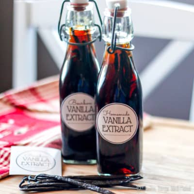 Close-up of two bottles filled with homemade vanilla extract, with fresh vanilla beans next to them.