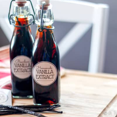 Two bottles of homemade vanilla extract with vanilla beans next to them.