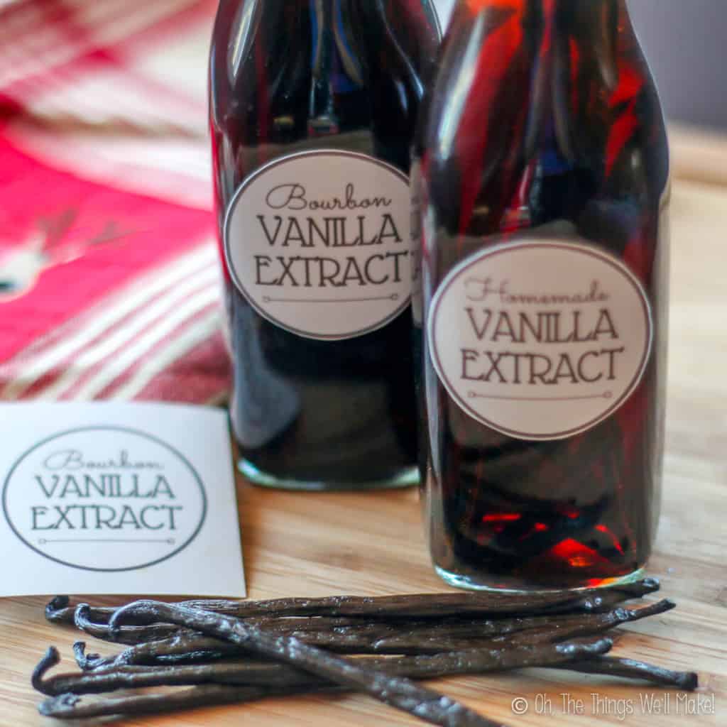 Closeup of two bottles of homemade vanilla extract with some vanilla beans next to them. There is also a vanilla extract label next to them.