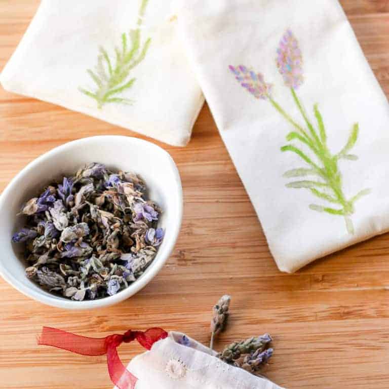 A cup of lavender next to two homemade cream colored lavender sachets with lavender print on them.