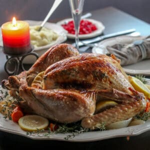 A roasted turkey on a platter garnished with lemon slices, thyme, and roasted vegetables.