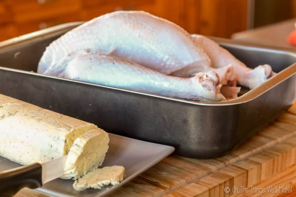 turkey in roasting pan along side a log of compound butter.