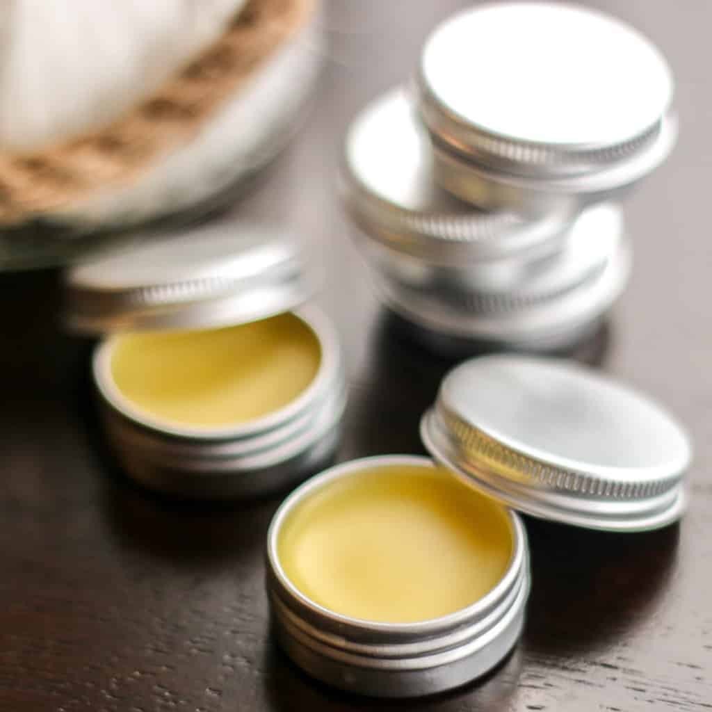 Close-up of solid perfume tin cans. Two cans open showing the solid perfume inside while three cans are stacked one on top of the other at the back.