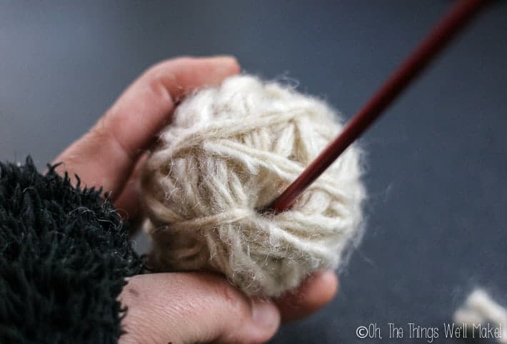 Using a stick to poke the free end of the wool yarn into the center of the ball of wool.
