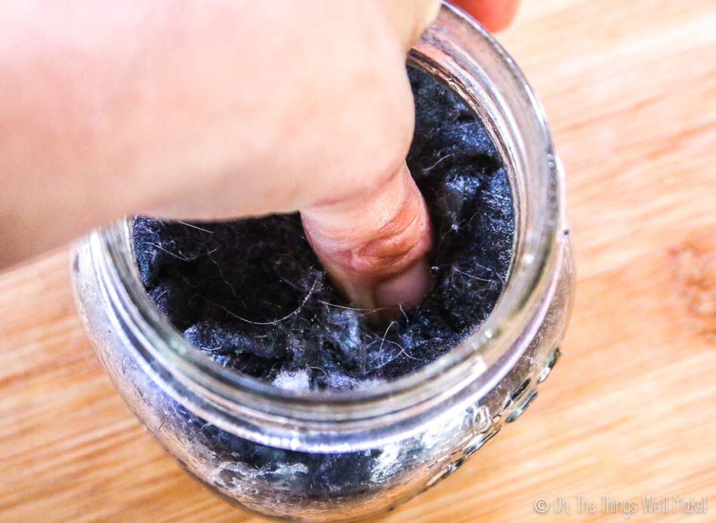 A thumb pressing into dryer lint in a glass jar