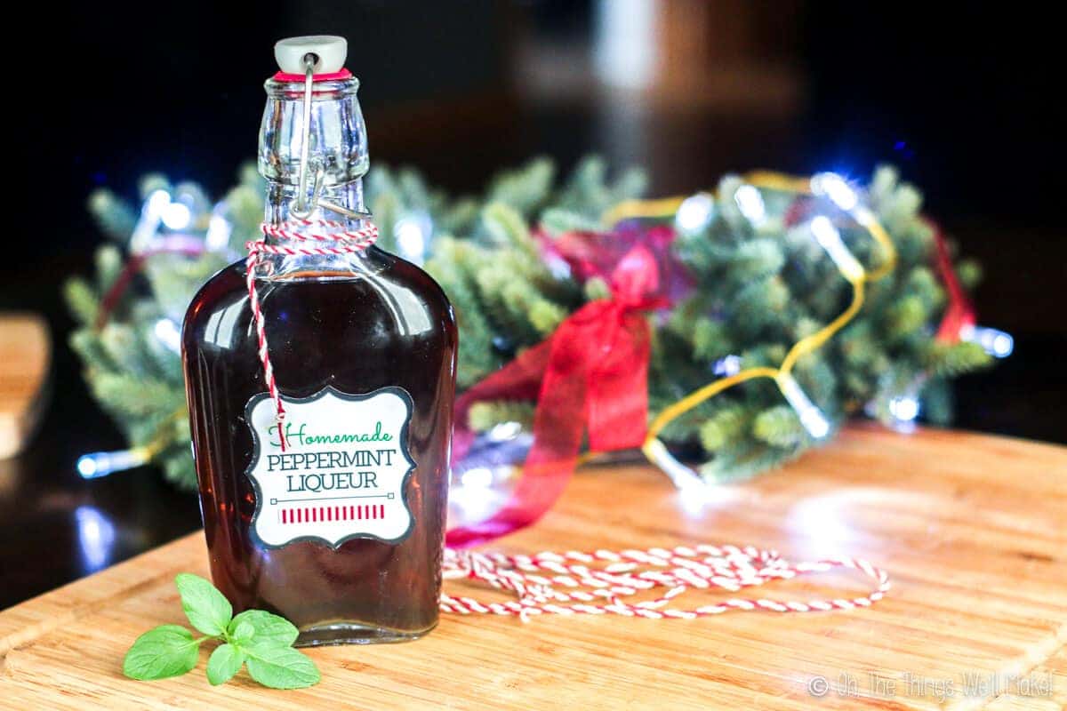 A bottle of homemade peppermint liqueur wrapped in bakers twine with a sprig of fresh mint.
