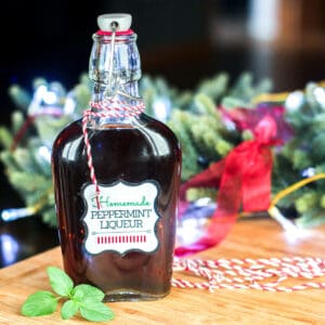 A bottle of homemade peppermint liqueur wrapped in bakers twine with a sprig of fresh mint.