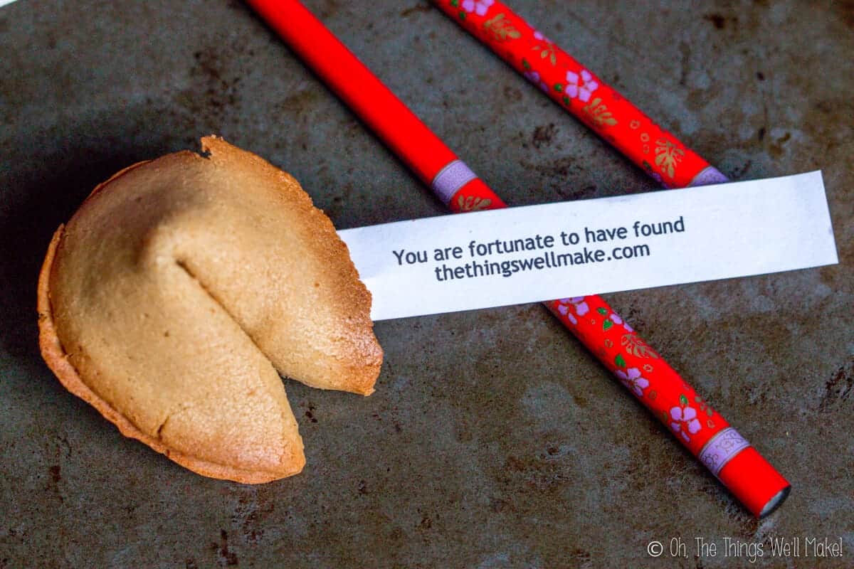 Overhead view of a homemade fortune cookie with a fortune coming out of it that reads "You are fortunate to have found thethingswellmake.com" over red chopsticks.