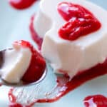 Scooping up a heart-shaped homemade panna cotta with strawberry puree on a spoon
