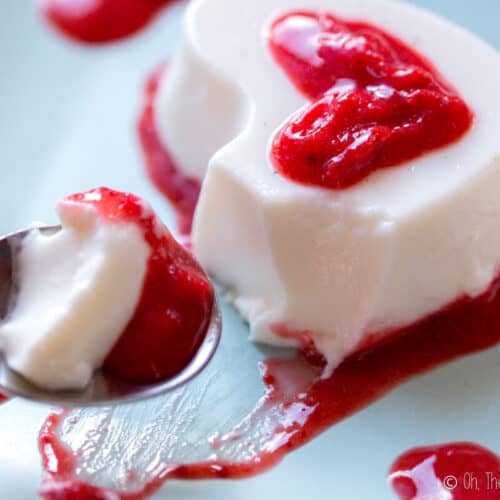 Scooping up a heart-shaped homemade panna cotta with strawberry puree on a spoon